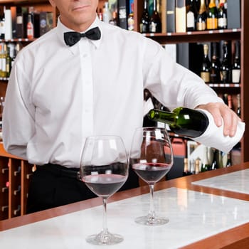 Waiter pouring red wine into wine glasses in a bar