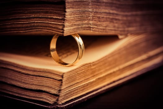 Golden ring between the pages of old book in vintage style, close up, soft focus
