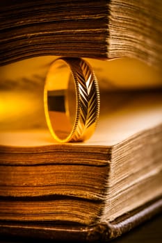 Golden ring between the pages of old book in vintage style, close up, soft focus
