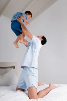 Mid adult man playing with his son on the bed