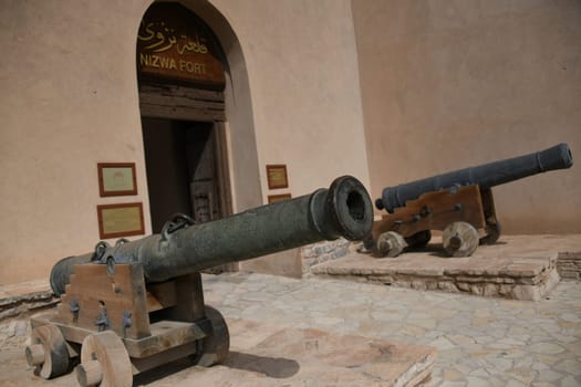 The large fortress Fort Nizwa is located on the edge of the Hajar Mountains in the oasis city in Oman. There are two ancient conons at the entrance to the fortress.