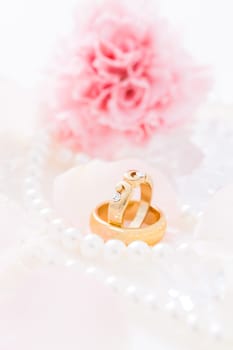 Golden wedding rings with pearl necklace wih pink flower in the background, soft focus