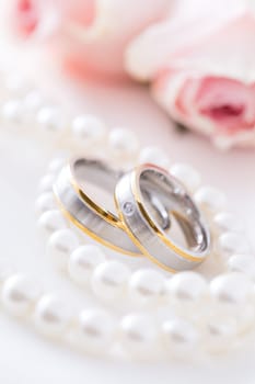 Modern wedding rings with pearl necklace wih pink roses in the background, soft focus