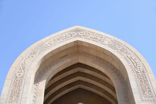Archway with the Arabic inscription Great Sultan Qaboos Mosque and the main minaret in a visual axis. It is considered to be one of the most important buildings in the Sultanate of Oman.