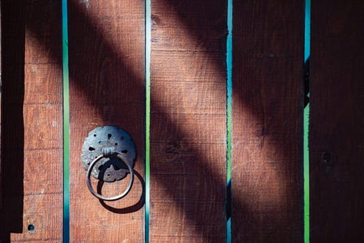 Detail of old wooden door with metal handle on planks. Dark brown door in vintage and antique style. Exterior and facade.