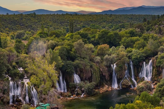 Kravice Waterfalls with mountains, sunset sky and clouds in background., Bosnia and Herzegovina, Europe. Summer travel.