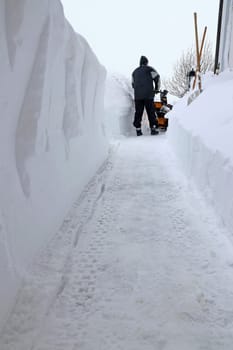 A man clears the sidewalk with a snow blower during heavy snowfall