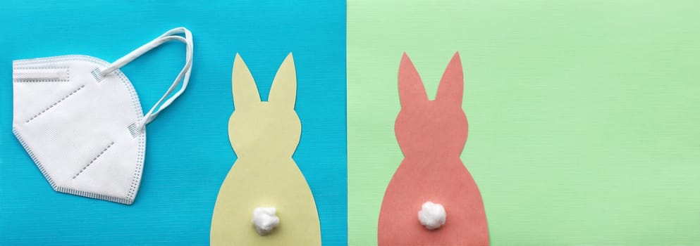 Corona and Easter. FFP2 protective mask and two paper Easter bunnies on a green and blue background