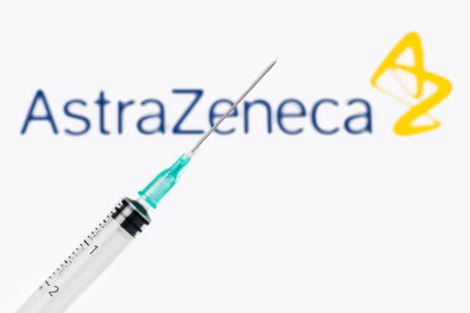 Teo, Spain  January 25, 2021: AstraZeneca Covid-19 vaccine concept. Close-up of a syringe over the AstraZeneca company logo blurred in the background.