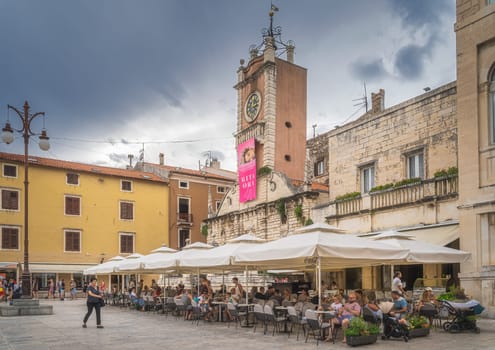 Zadar, Croatia, July 2019 Tourists relaxing in outdoor restaurant and beer garden in the square of old town with St. Lawrence Church in background