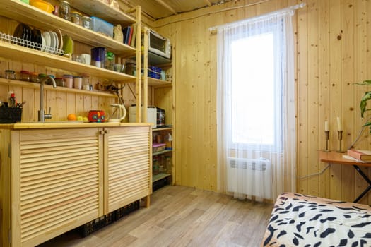 The interior of a small kitchen in a country cottage, the walls are decorated with wooden clapboard