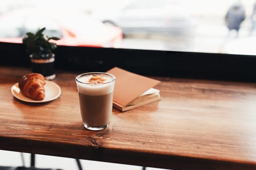 Cup of coffee, croissant, notebook at table in cafe. Blurred background. High quality photo