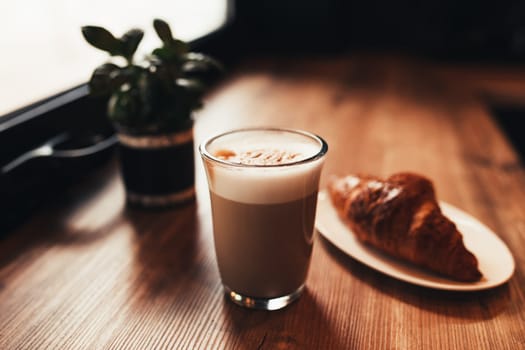 Cup of coffee, croissant at table near the window in cafe. Blurred background. High quality photo