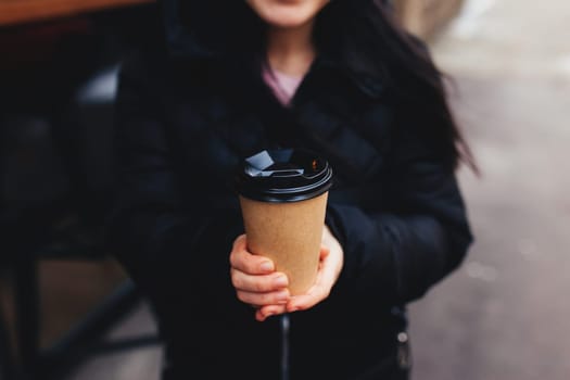Girl holds a paper cup of coffee in hand near cafe. High quality photo