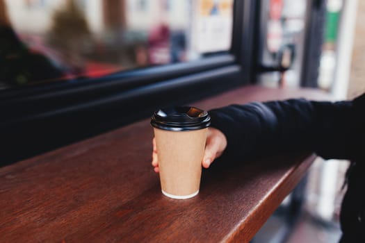 Girl holds a paper cup of coffee in hand near cafe. High quality photo