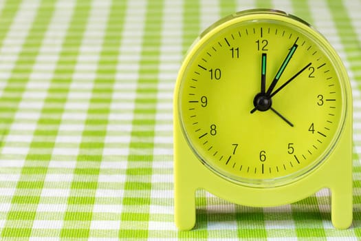 Green alarm clock on the table with checkered tablecloth