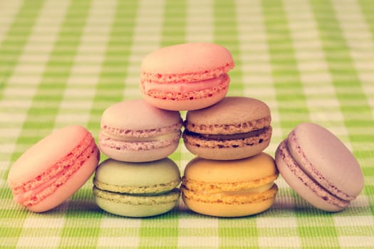 French delicious dessert macaroons stacked on checkered tablecloth, vintage tone