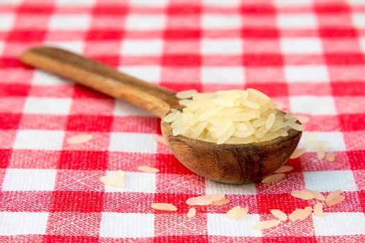 Raw parboiled rice in a wooden spoon on checkered tablecloth