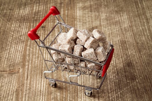 Shopping cart full of brown cane sugar on wooden background