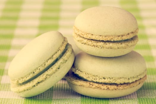 Three green macaroons stacked on checkered tablecloth, vintage tone