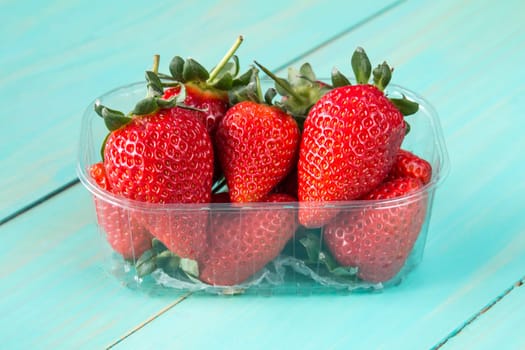 Plastic box full of red strawberries on the blue wooden background