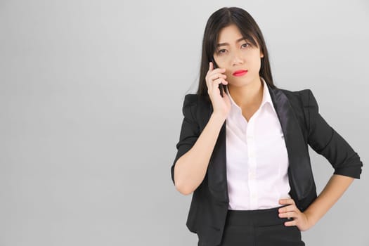 Young Asian women in suit standing posing using her phone against gray background