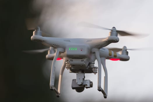 Great Malvern, United Kingdom, 27th December, 2020: Drone quadcopter hovering in front of trees and blue sky, selective focus blurs the background