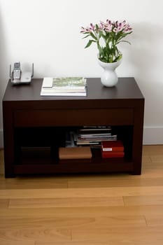 Flower vase with books and a cordless phone on a side table