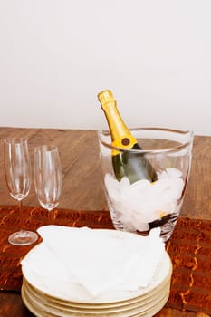 Champagne bottle in an ice bucket with champagne flutes and plates on a table