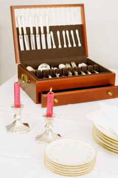 Two burning candles with a cutlery box and stacks of plates on a dining table