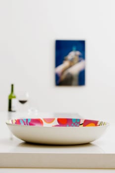 Close_up of a bowl on a dining table with a bottle of red wine in the background