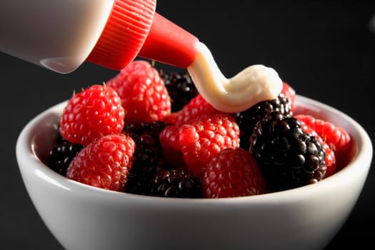 Close-up of raspberries and blackberries in a bowl with cream poured on top
