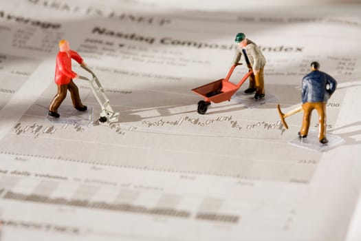 Figurines of manual workers working on a financial newspaper