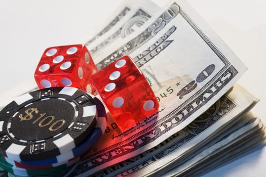 Two dices with a gambling chip on a stack of US dollar bills