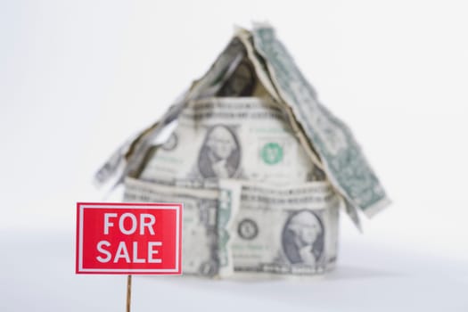 For Sale board in front of a miniature house made up of US dollar bills