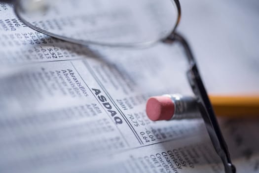 Close_up of a pencil with eyeglasses on a financial newspaper