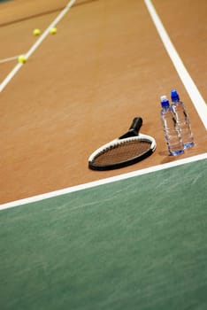 Tennis racket with two water bottles on a tennis court