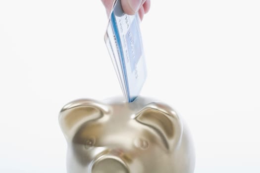 Close_up of a personŽs hand putting a credit card into a piggy bank