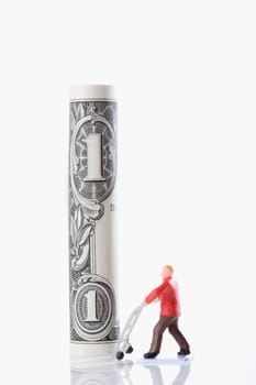 Figurine of a manual worker carrying a rolled up US paper currency on a push cart