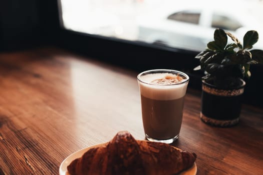 Cup of coffee, croissant at table near the window in cafe. Blurred background. High quality photo