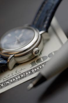 Close-up of a wristwatch with a pen on an one hundred dollar bill