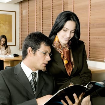 Businessman and a businesswoman sitting in an office and looking at a magazine