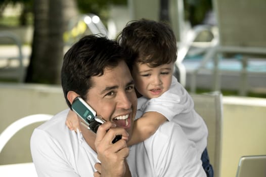 Close-up of a father talking on a mobile phone with his son hugging from behind