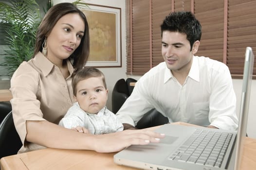 Portrait of a baby boy sitting in front of a laptop with his parents