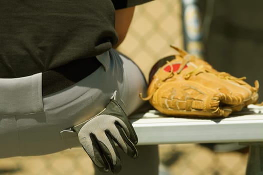 Mid section view of a person sitting on a bench with a baseball glove
