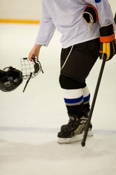 Side profile of an ice hockey player holding an ice hockey skate and a helmet