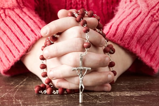 Hands of a young Christian child holding  rosary with cross