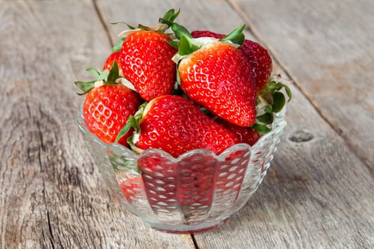 Fresh juicy strawberries in glass bowl on wooden background