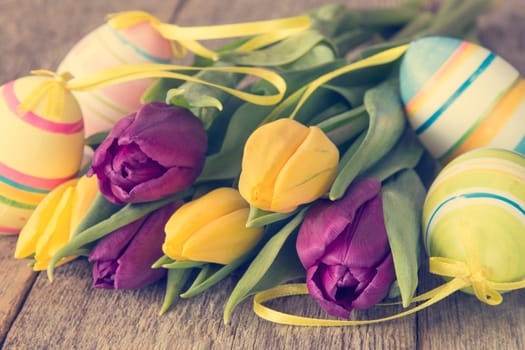 Bouquet from yellow and purple tulips with Easter eggs on wooden background