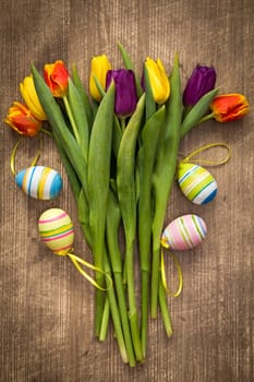 Easter eggs and colorful tulips bouquet on wooden background